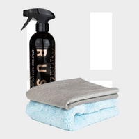 Een zwarte RUSH Spray Wax fles met het label RUS staat naast een grijze doek en een blauwe handdoek, klaar om glanzen te auto laten met een beschermende laag.