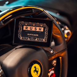 A RUSH gift card in a black case rests on the steering wheel of a Ferrari, with the yellow Ferrari logo clearly visible in the foreground.