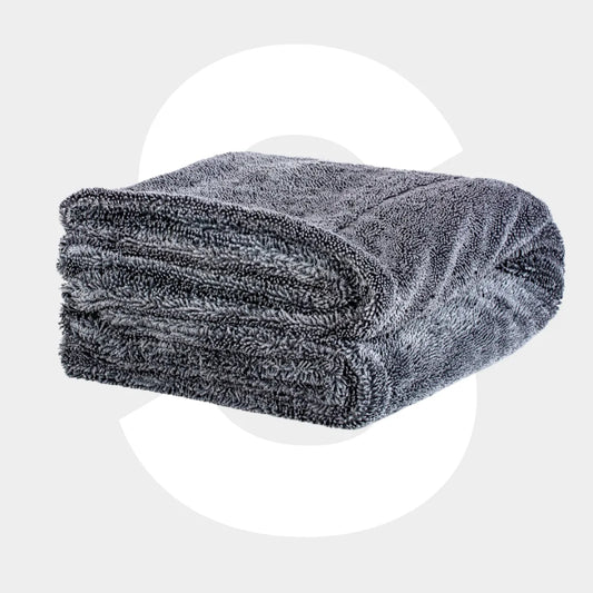 A neatly folded Master Drying Towel 1600 GSM XL, dark gray with a soft, textured surface, is set against a light gray background with a large, faint white letter C behind it.