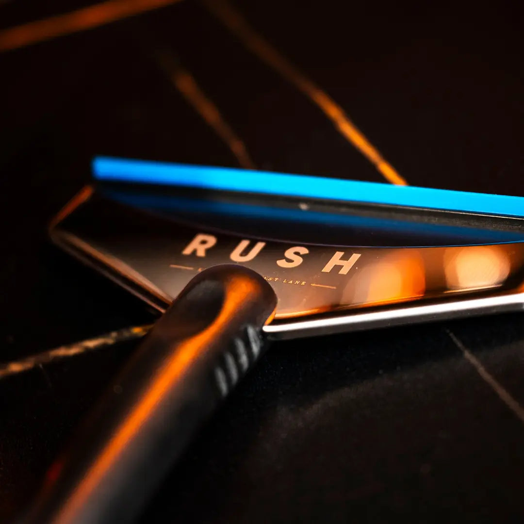 Een zwart met blauwe RUSH Window Clear Winter Kit zuigmond rust op een donker, reflecterend oppervlak met oranje lichtreflecties.