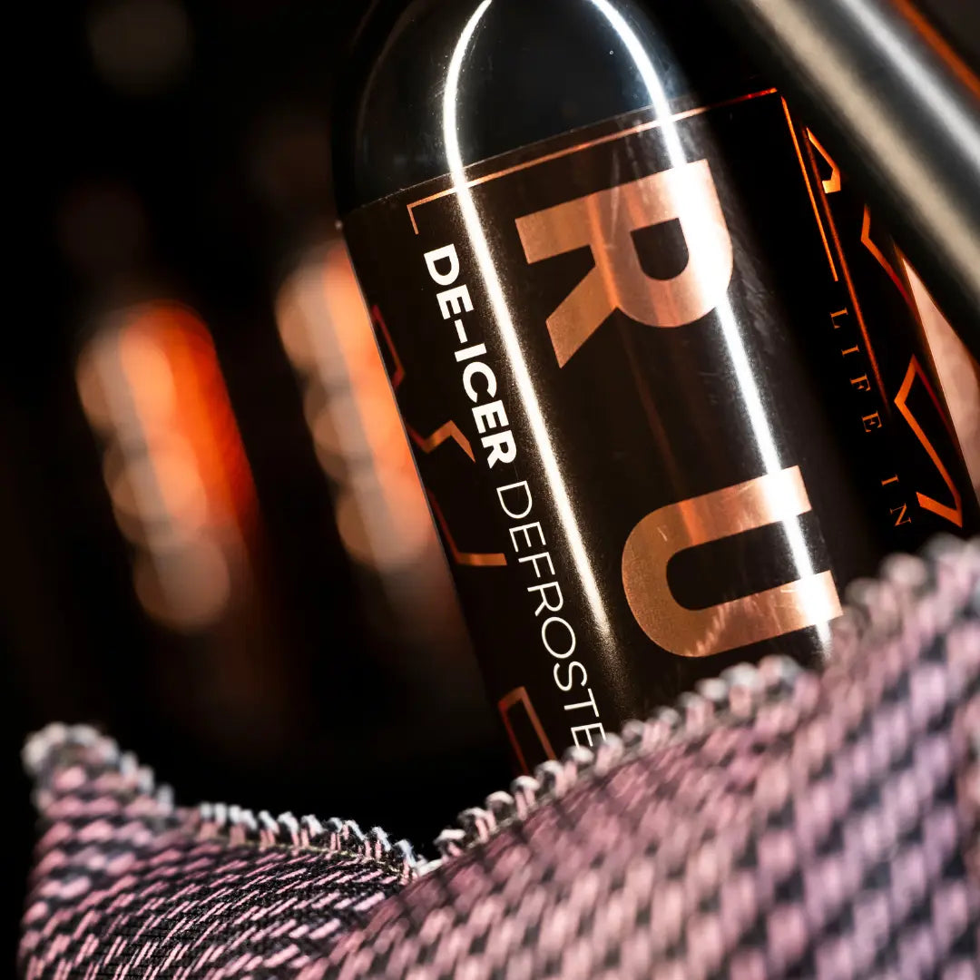 Een close-up van een De-Icer DEFROSTER fles in een zwart-roze stoffen houder uit de RUSH Window Clear Winter Kit.