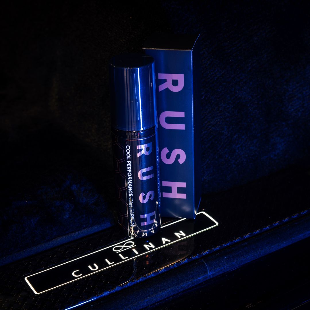 Een fles en doos met het label RUSH Cool Performance autoparfum rusten op een verlichte CULLINAN auto dorpel, tegen een donkere achtergrond.