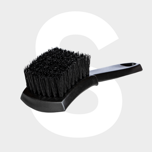The Tire Brush, featuring a black design with stiff bristles and a curved handle for optimal banden reinigen, is shown on a light gray background with a large white letter S behind it.