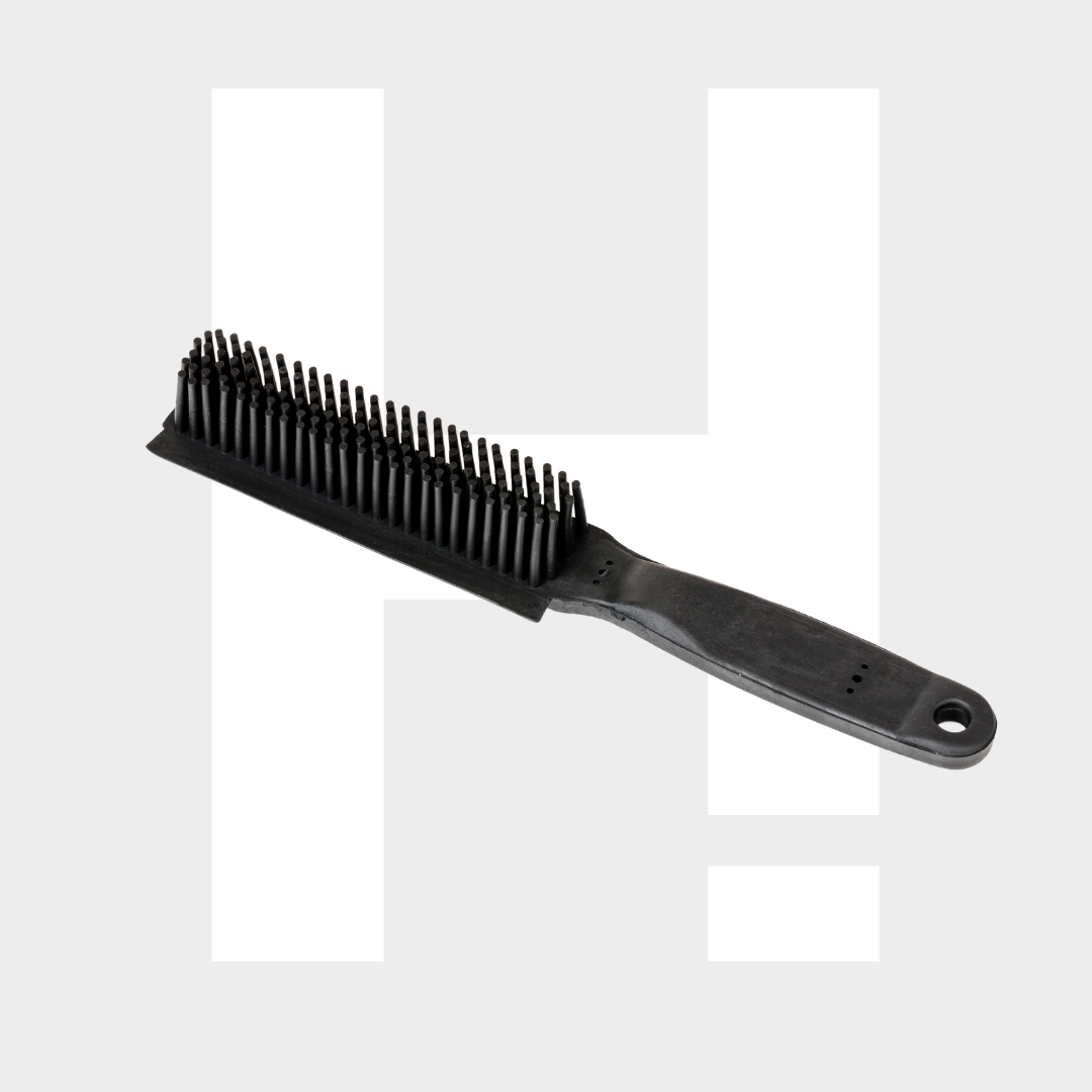 Een zwarte draadharen borstel met een plastic handvat voor hondenharen verwijderen ligt op een lichtgrijze achtergrond met een grote witte letter H.
