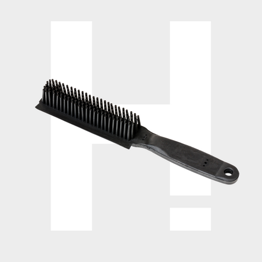 Een zwarte draadharen borstel met een plastic handvat voor hondenharen verwijderen ligt op een lichtgrijze achtergrond met een grote witte letter H.