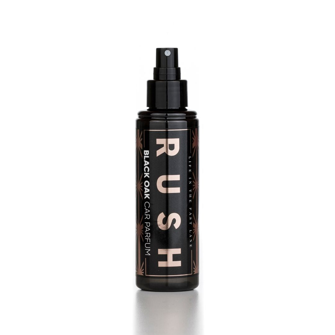 Een zwarte autoparfum sprayfles met het label RUSH BLACK OAK CAR PARFUM staat rechtop op een witte achtergrond.
