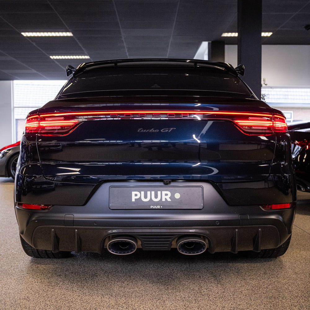 Achteraanzicht van een zwarte Porsche Turbo GT die binnen geparkeerd staat, met dubbele uitlaatpijpen, achterlichtstrip en een detailingpad bij de bumper.