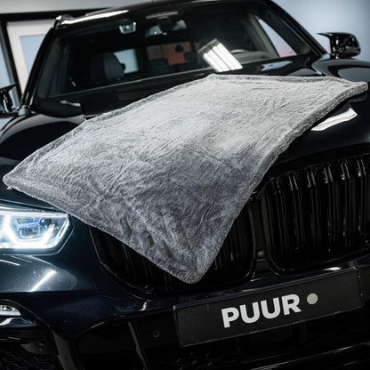 A Master Drying Towel 1600 GSM XL is draped over the hood of a shiny black car with lit headlights; the car's front grille and PUUR license plate are visible.