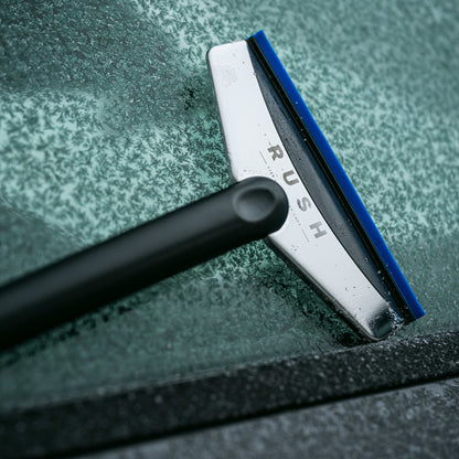 Een close-up van een RUSH Window Clear Winter Kit IJskrabber die rijp van de voorruit van een auto verwijdert.