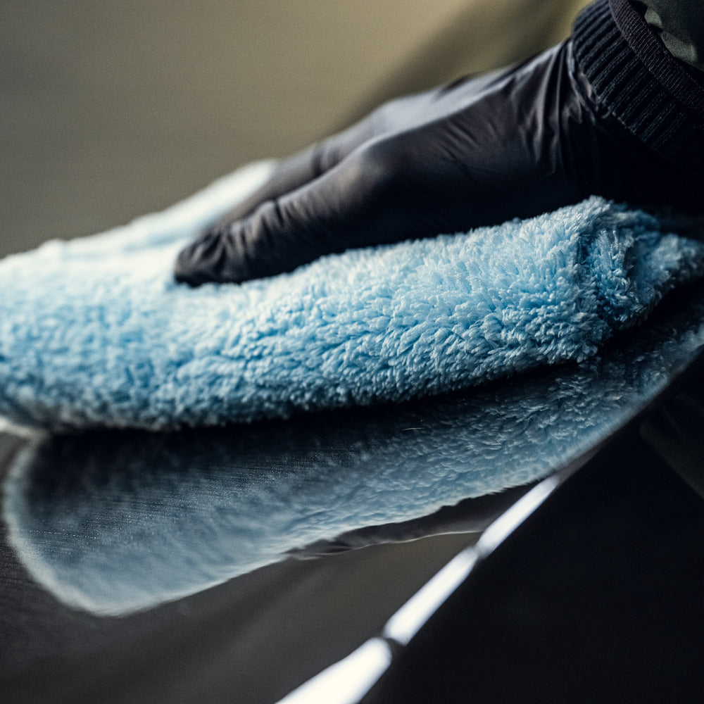 Een gehandschoende hand gebruikt een ultrazachte microvezeldoek om een glad, reflecterend oppervlak schoon te maken of te polijsten.