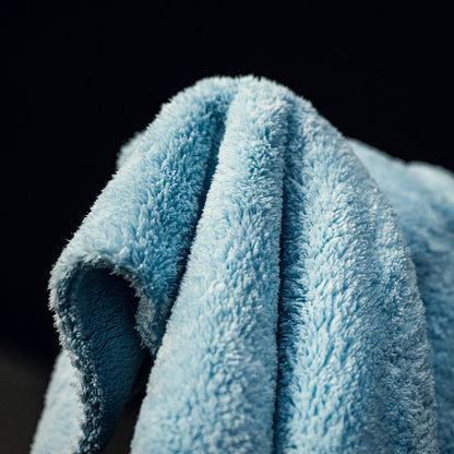 Een close-up van een lichtblauwe, ultrazachte microvezeldoek gedrapeerd over een oppervlak, tegen een donkere achtergrond.