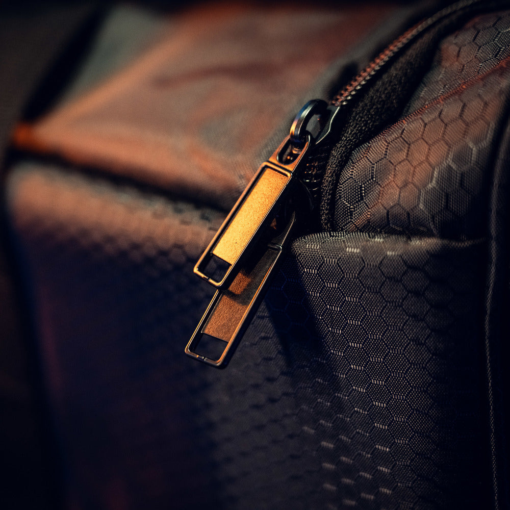 Close-up van twee metallic ritsen op een RUSH Detailing Bag, een ruime opbergtas met donkere stof met zeshoekpatroon.