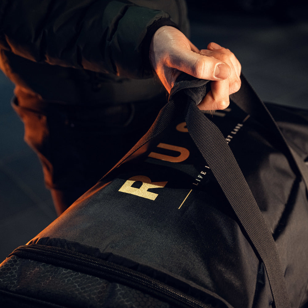 Een persoon in een donkere jas houdt een RUSH Detailing Bag vast, een ruime opbergtas die perfect is voor schoonmaakproducten opbergen.