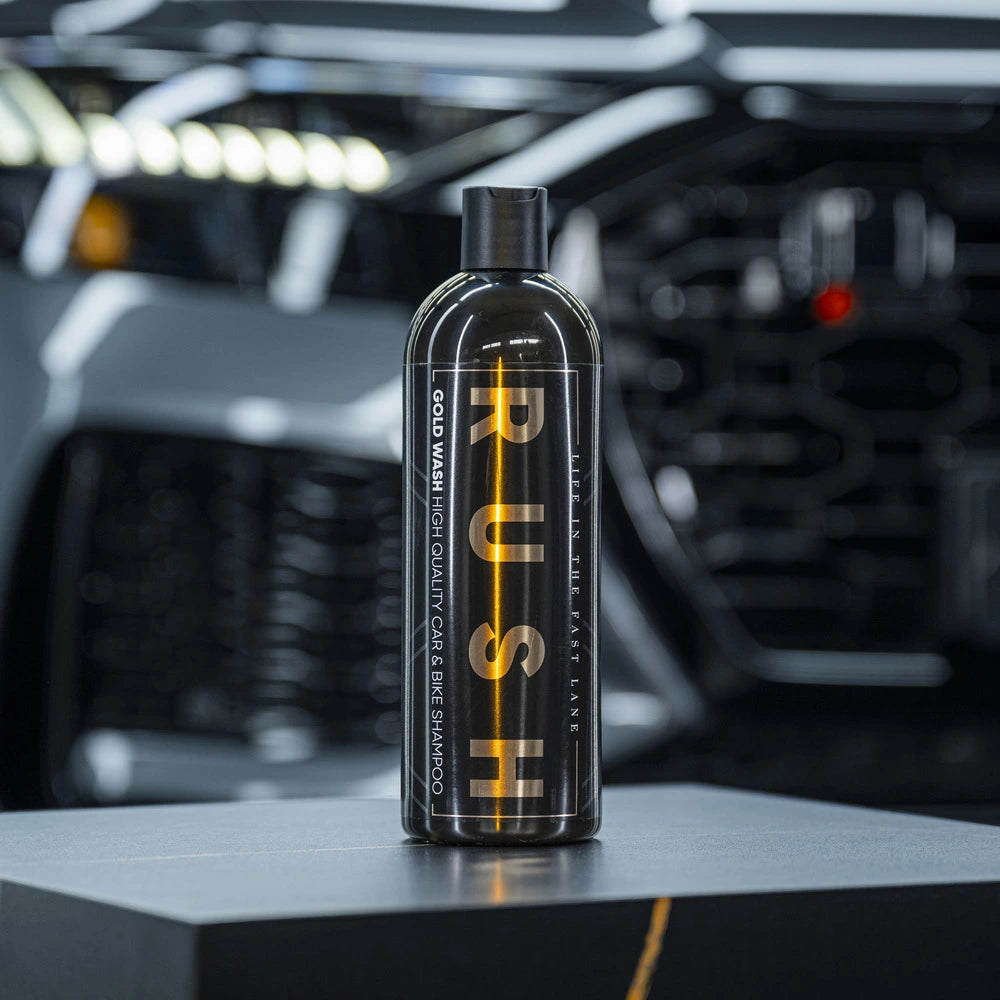 Een zwarte PUSH-fles voor autoshampoo staat op een donker oppervlak, met een wazige voorkant van een auto op de achtergrond, klaar om te eikelen en te autowassen.