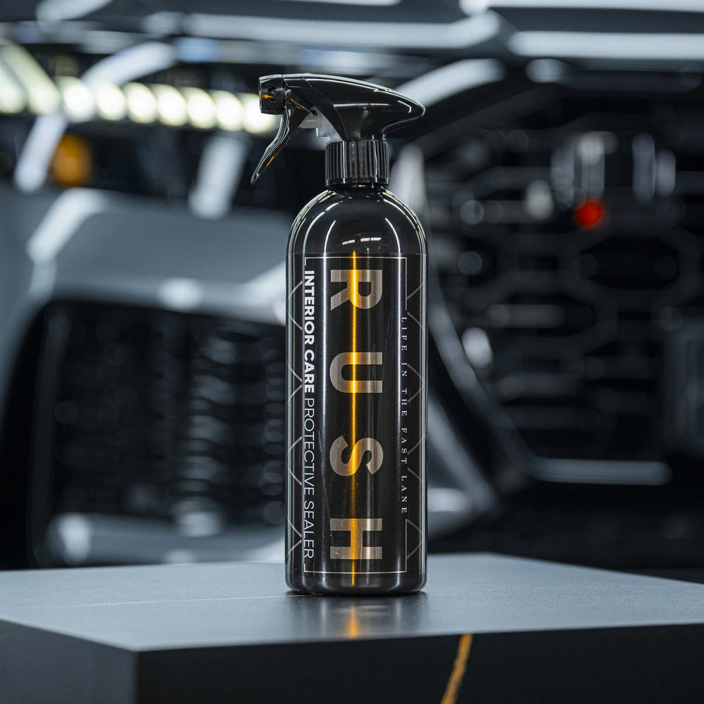Een zwarte interieurverzorgingsspray met het label PUSH staat op een donker oppervlak, met daarachter een wazig auto-interieur, ideaal voor interieur beschermen auto.