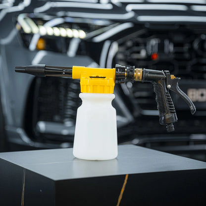 A black and yellow Foam & Water Spray Gun with a white soap bottle is displayed on a dark pedestal, the blurred front grill of a black vehicle in the background—perfect for use without a pressure washer.
