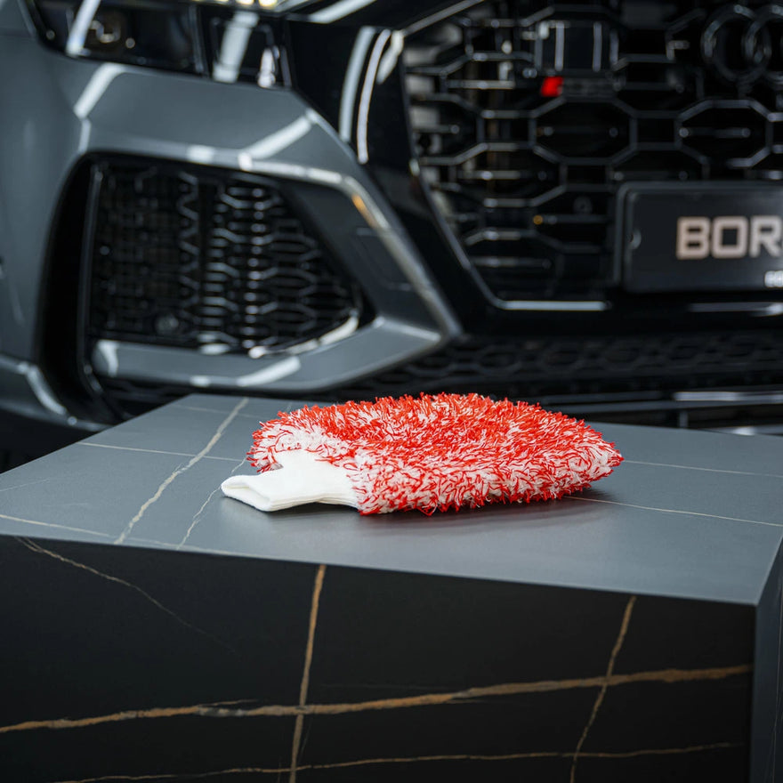 Een rood-witte microvezel washandschoen met groot absorberend vermogen rust op een donker, marmeren oppervlak bij een grijze auto.