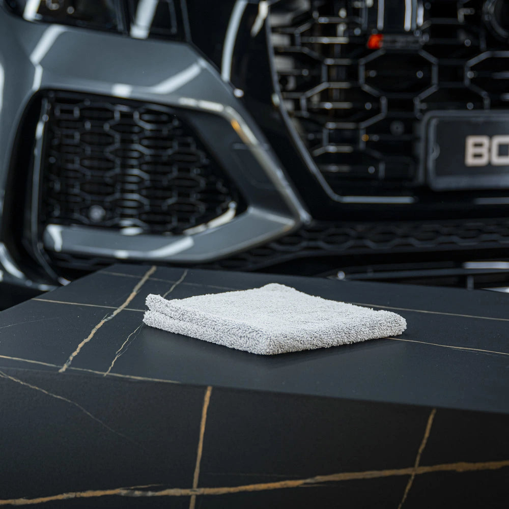 Een opgevouwen RUSH Allround Interior Cloth ligt op zwart marmer, perfect voor interieur reinigen auto met een autorooster op de achtergrond.
