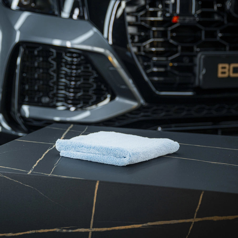 Een gevouwen ultrazachte microvezeldoek 500 GSM vlies ligt op donker marmer, met een deel van een autogrille zichtbaar op de achtergrond.