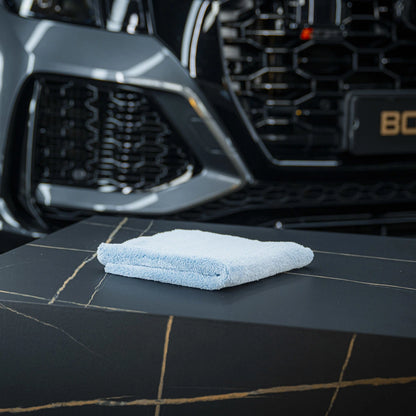 Een gevouwen ultrazachte microvezeldoek 500 GSM vlies ligt op donker marmer, met een deel van een autogrille zichtbaar op de achtergrond.