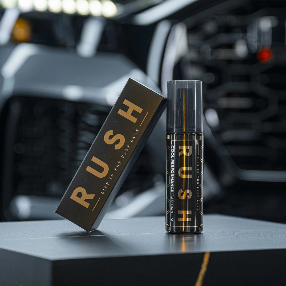 Een flesje en het doosje met het label RUSH Cool Performance auto parfum worden getoond op een plat oppervlak met een auto-interieur onscherp op de achtergrond.