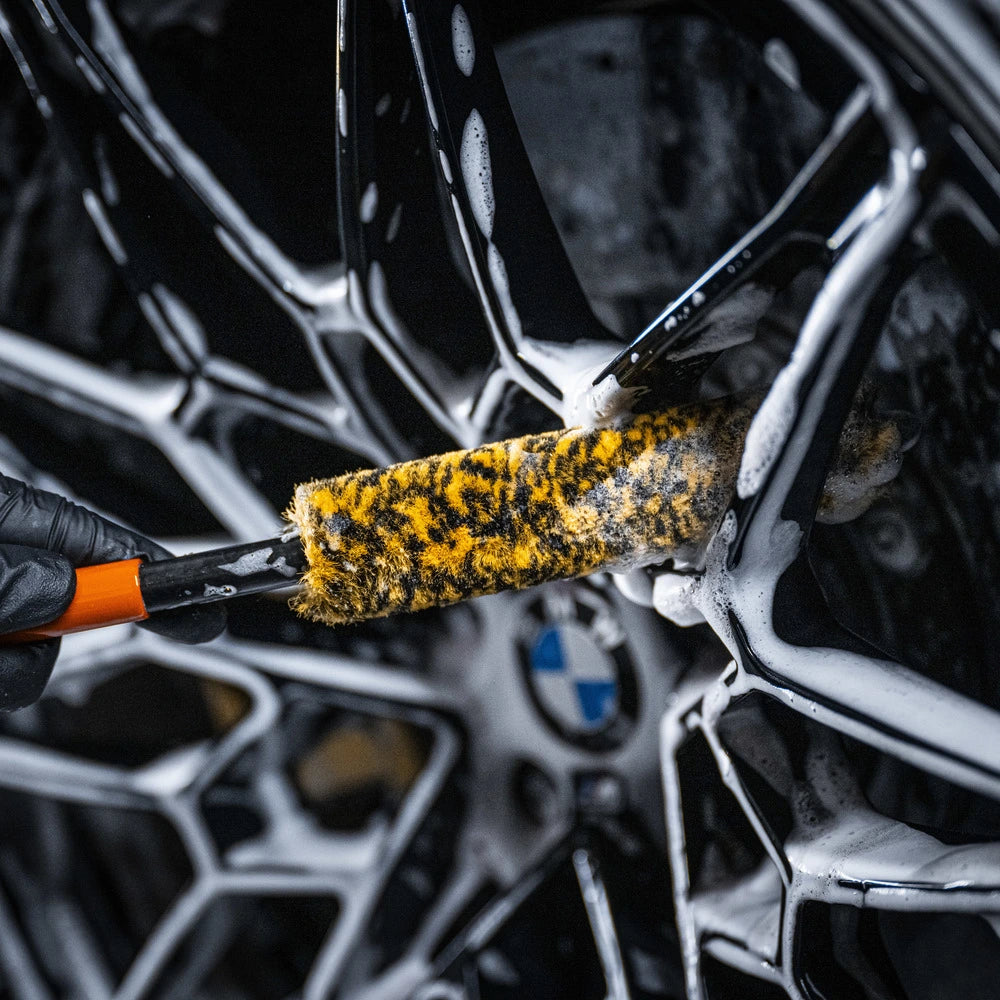 A close-up of a gloved hand cleaning a soapy BMW wheel rim with the Wheel Woolie Small, perfect for spaakvelgen reinigen.