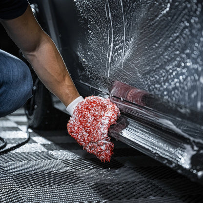 Een persoon met een rood-witte microvezel washandschoen maakt de onderkant van een zeepachtige autodeur schoon.