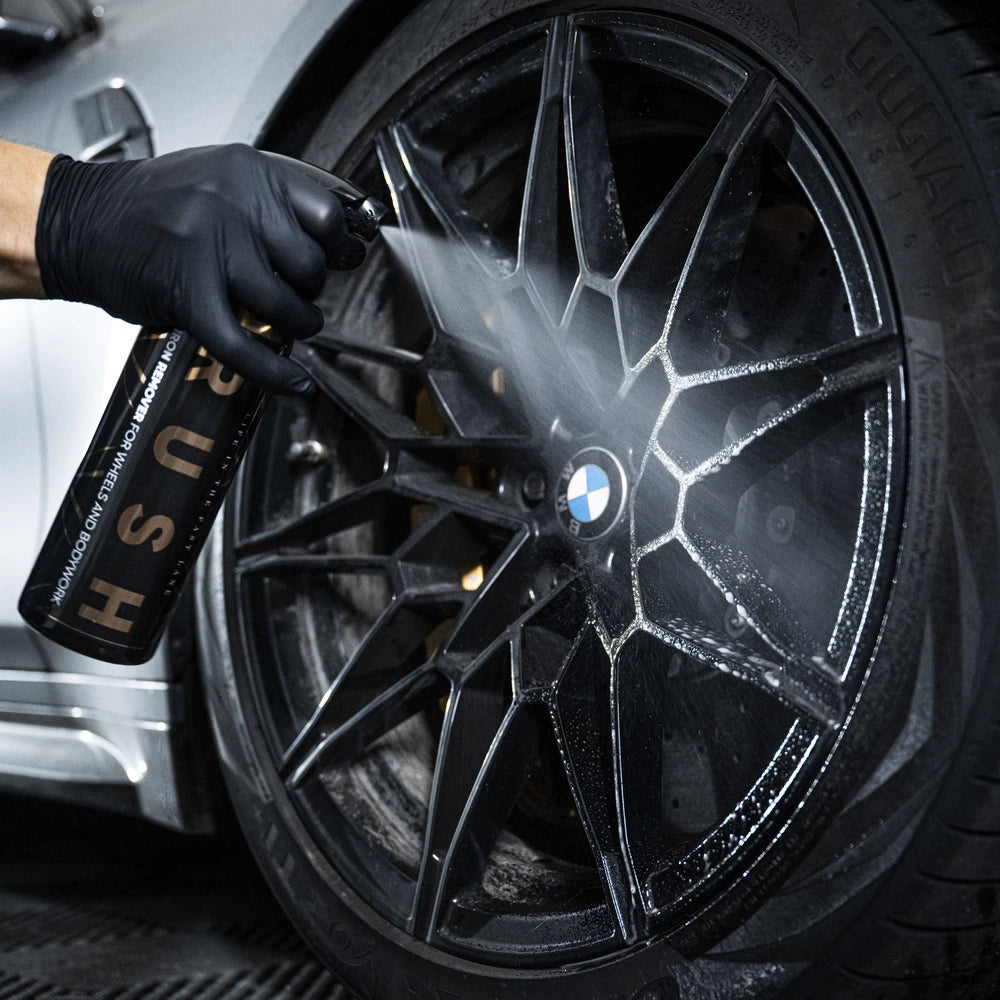 Een gehandschoende hand spuit ijzerverwijderaar op een zwarte BMW velg, waarbij zich zichtbaar schuim vormt op de spaken.