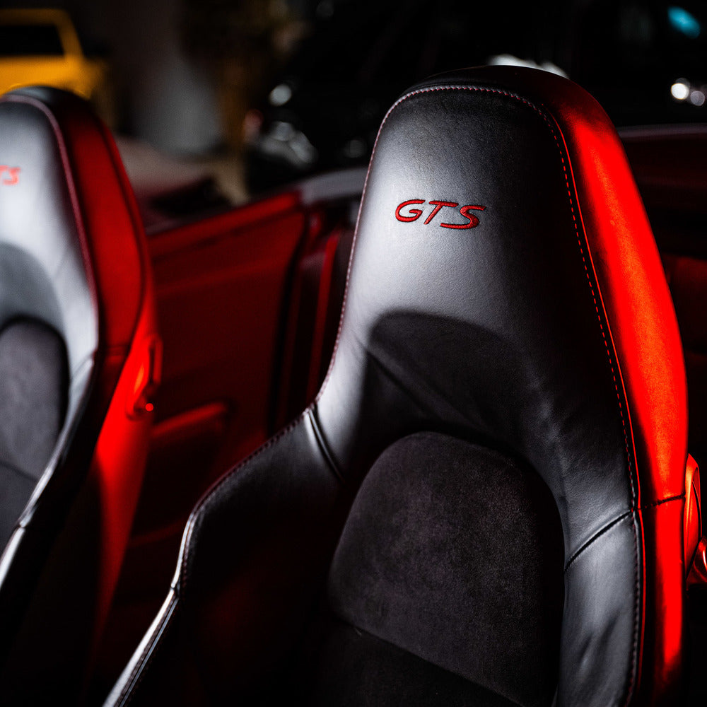 Close-up van lederen autostoelen met GTS geborduurd in rood stiksel, verlicht door rood omgevingslicht.