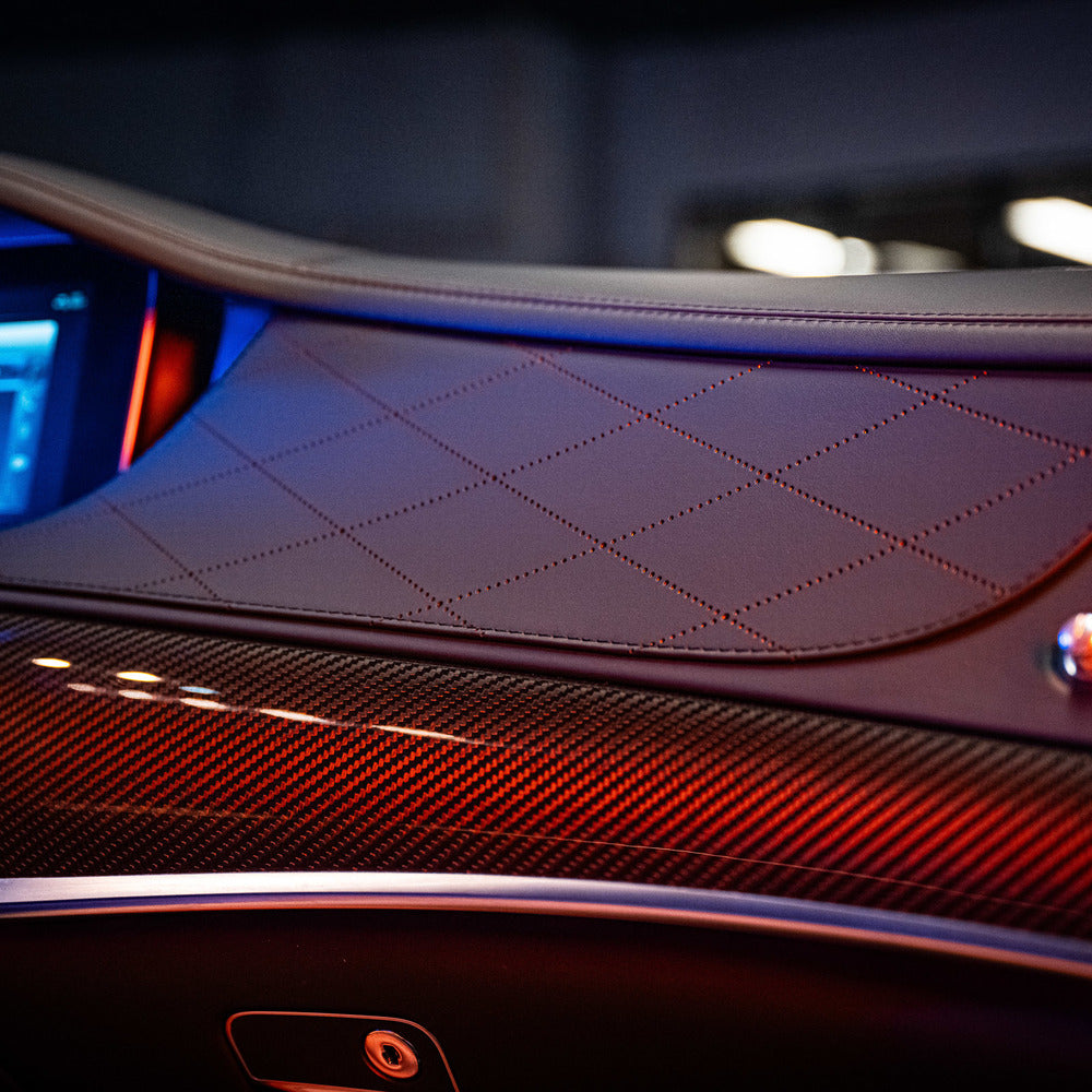 Close-up van een autodashboard met gewatteerd leer, koolstofvezel panelen en sfeerverlichting - perfect voor interieur beschermen auto.