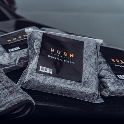Drie verpakte grijze droogdoeken 600 GSM met het label RUSH worden weergegeven op een donker, glanzend oppervlak - perfect als droogdoek auto.