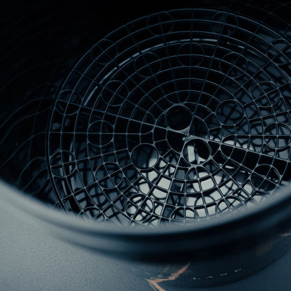 Een close-up van een zwarte ronde gritbeschermer in een detailingemmer, mogelijk gebruikt voor autowassen of keukenapparatuur.