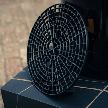 Een ronde zwarte gritbeschermer rust op een donker betegeld oppervlak, perfect voor gebruik in je auto wassen detailing emmer.