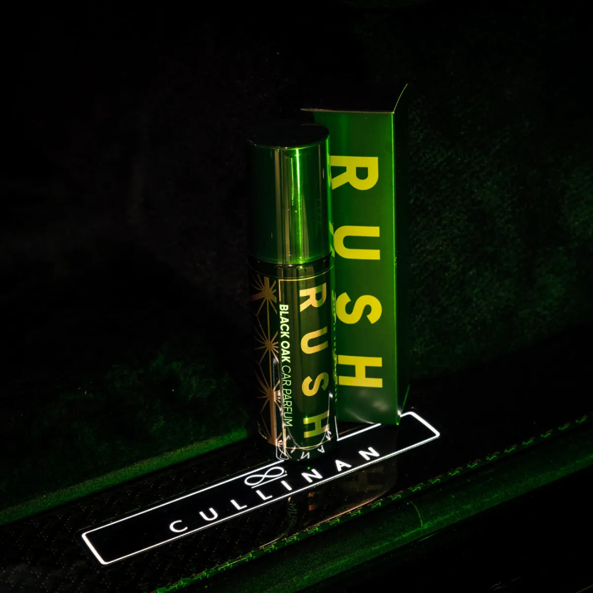 Een flesje en doosje Rush Black Oak Cardamom auto parfum staan uitgestald op een oppervlak met het label Cullinan, verlicht met groen licht.
