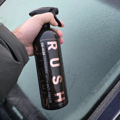 Een persoon houdt een RUSH Window Clear Winter Kit De-Icer sprayfles naast een matte autoruit.