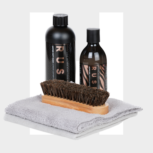 The Leather Clean & Care Package includes two RUS shoe cleaning bottles for leather care, a wooden brush with dark bristles, and two gray towels, all arranged together on a light background.