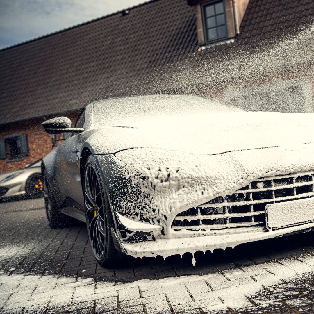 Een auto bedekt met dik sneeuwschuim wordt gewassen op een verharde oprit voor een bakstenen huis.