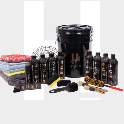 The Starter Kit XXL | 25-delig is a premium car cleaning set with black "RUSH" bottles, brushes, sponges, and microfiber towels, all neatly arranged around a large black bucket on a light gray background.