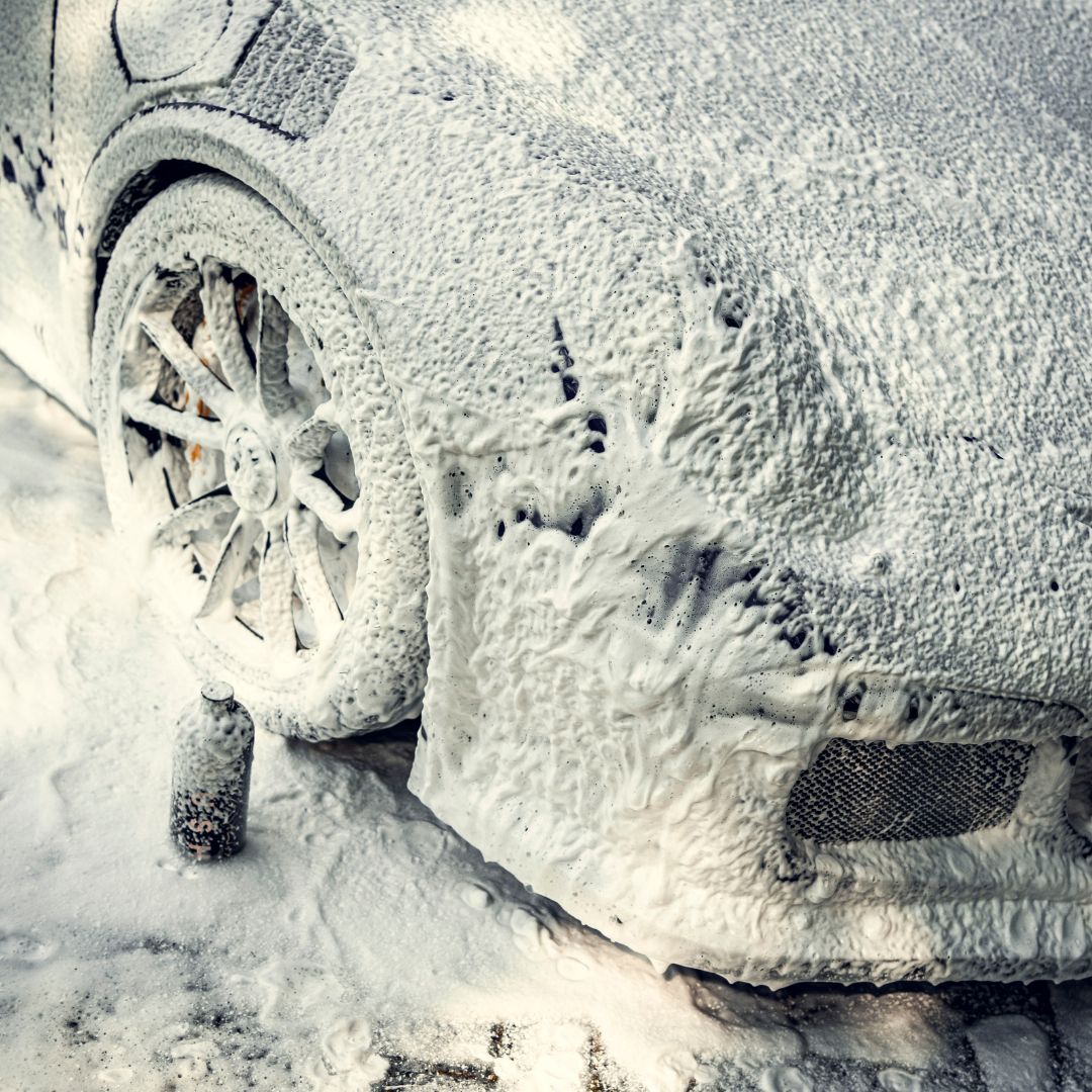 Een auto bedekt met dik sneeuwschuim, met de nadruk op het voorwiel en een deel van de carrosserie, tijdens een intensieve autowasbeurt.