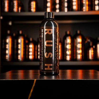 Een zwarte fles met het label RUSH De-Icer staat op een toonbank, onderdeel van de RUSH Window Clear Winter Kit, met soortgelijke flessen op de achtergrond.
