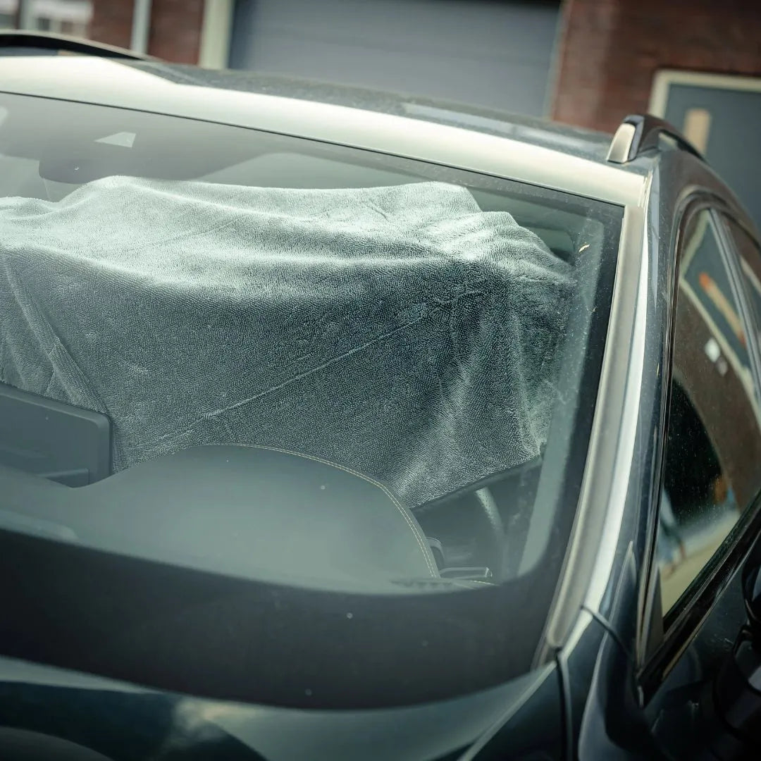 Blik door de voorruit van een auto met een grote grijze doek op het dashboard, klaar voor gebruik met de RUSH Window Clear Winter Kit of IJskrabber De-Icer.