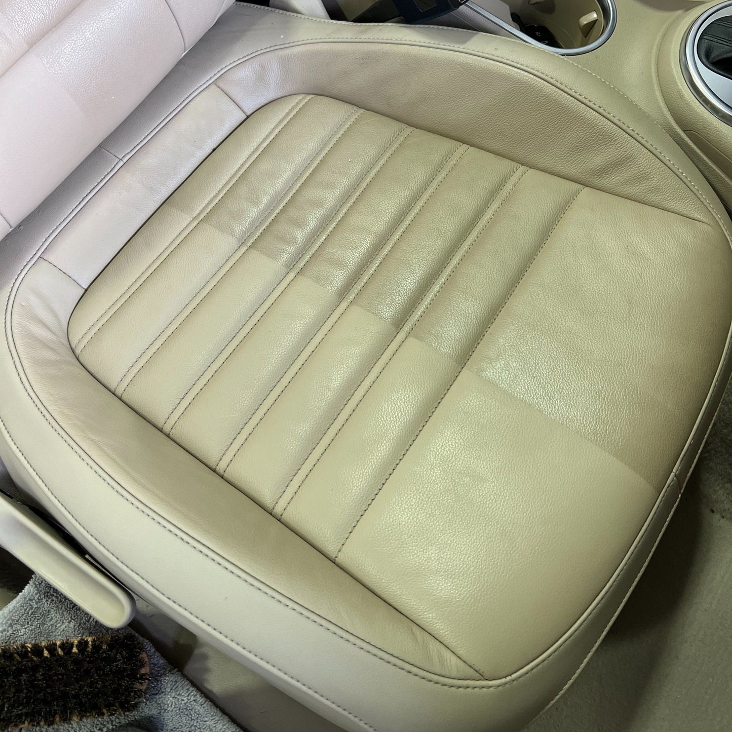 Close-up of a beige leather car seat with clean, smooth surface, visible creases and stitching—achieved by using Leather Matt Clean. The matte finish stands out beside cup holders in the car’s interior.
