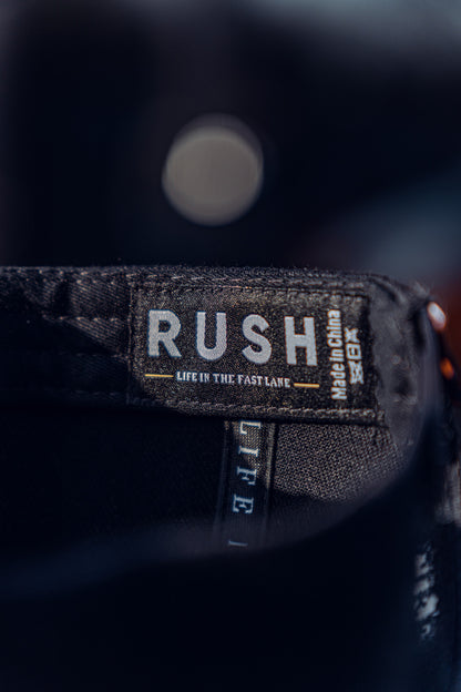 Close-up of the RUSH Baseball Cap's black fabric label, showing the brand name in bold white, "Life in the fast lane" beneath, and Made in China on the side. This adjustable cap ensures a perfect fit.